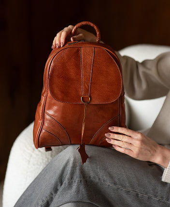 Brown leather backpack held by a person sitting on a white chair.
