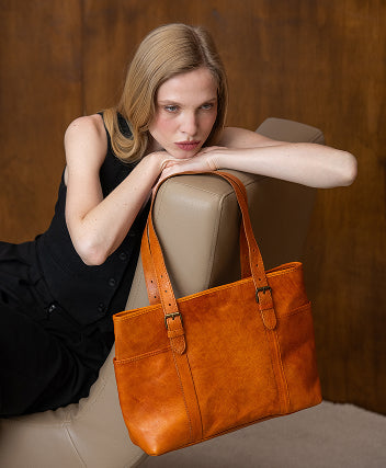 Woman holding an orange leather handbag against a wooden background